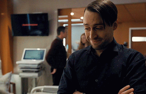 A Man Is Standing In A Hospital Room With His Arms Crossed And Smiling GIF