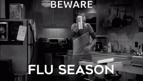 A Man Is Standing In A Kitchen Drinking From A Cup And Talking About Flu Season . GIF