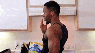 A Man Is Standing In A Kitchen With A Bag Of Raisins In His Hand . GIF
