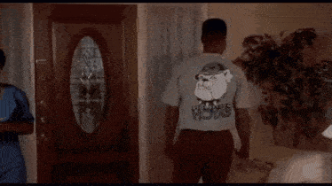 A Man Is Standing In A Living Room Wearing A T-Shirt With A Picture Of Santa Claus On The Back . GIF