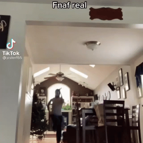 A Man Is Standing In A Living Room With A Ceiling Fan And A Sign On The Wall That Says Fnaf Real . GIF