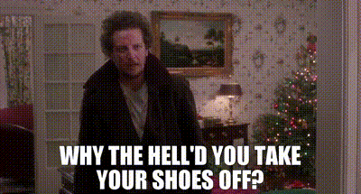 A Man Is Standing In A Living Room With A Christmas Tree In The Background And A Picture On The Wall . GIF