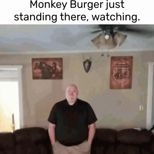 A Man Is Standing In A Living Room With A Monkey Burger Just Standing There Watching GIF
