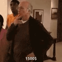 A Man Is Standing In A Living Room With A Woman And A Man Standing Behind Him . GIF