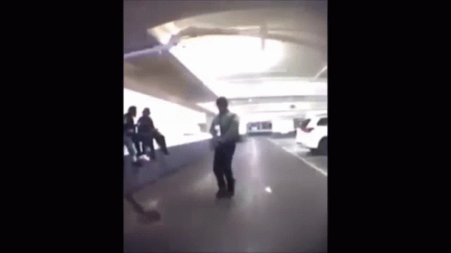 A Man Is Standing In A Parking Garage With A Group Of People Sitting On A Bench . GIF