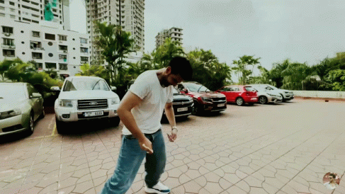 A Man Is Standing In A Parking Lot With A Ford Car Parked Behind Him GIF