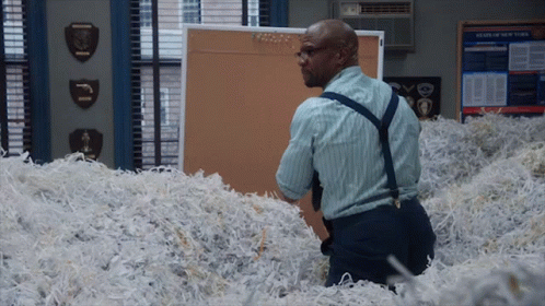 A Man Is Standing In A Pile Of Shredded Paper In Front Of A Bulletin Board That Says News Of New York GIF
