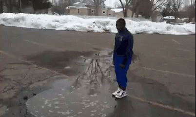A Man Is Standing In A Puddle Of Water On The Side Of A Road . GIF