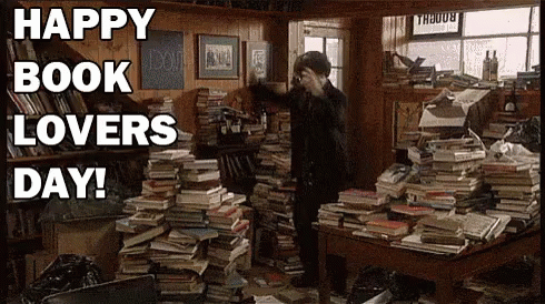 A Man Is Standing In A Room Filled With Lots Of Books And A Sign That Says Happy Book Lovers Day . GIF