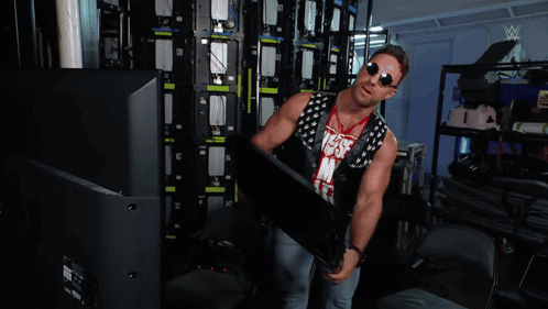 A Man Is Standing In A Room With A Wrestling Logo On The Wall GIF