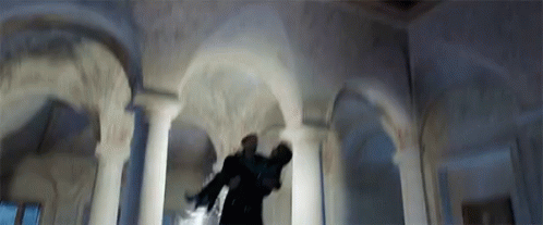 A Man Is Standing In A Room With Arches And Columns Holding A Gun . GIF