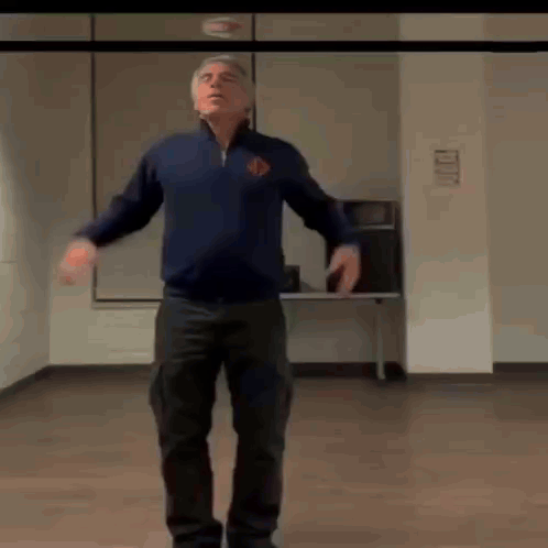 A Man Is Standing In A Room With His Arms Outstretched . GIF