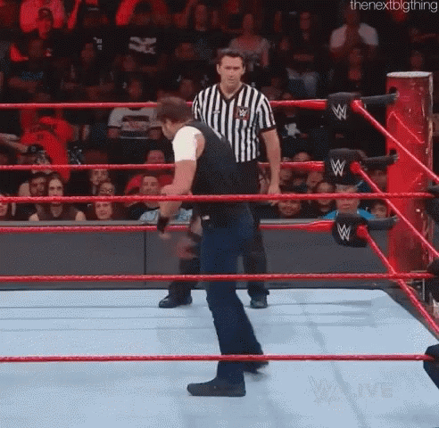 A Man Is Standing In A Wrestling Ring With A Referee In The Background . GIF