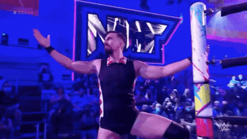 A Man Is Standing In A Wrestling Ring With His Arms Outstretched In Front Of A Crowd . GIF