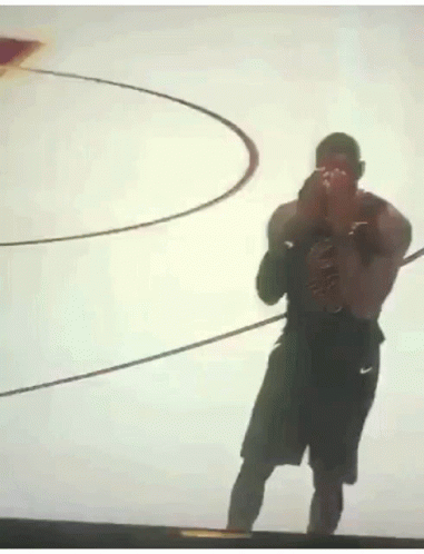 A Man Is Standing In Front Of A Basketball Hoop And Taking A Picture With His Phone . GIF