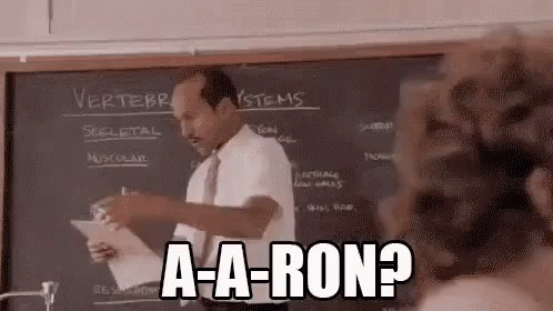 A Man Is Standing In Front Of A Blackboard Holding A Piece Of Paper And Saying `` A-A-Ron ? '' GIF