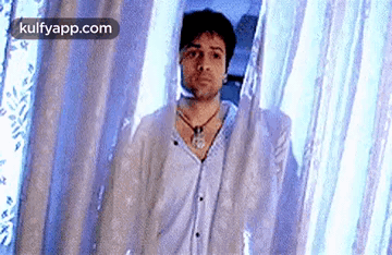 A Man Is Standing In Front Of A Blue Curtain And Looking At The Camera . GIF