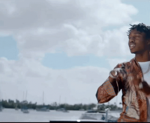 A Man Is Standing In Front Of A Body Of Water With Boats In The Background GIF