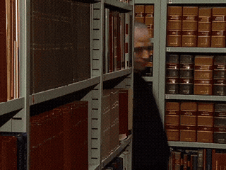 A Man Is Standing In Front Of A Bookshelf With A Book Titled ' A Brief History Of The World ' On It GIF