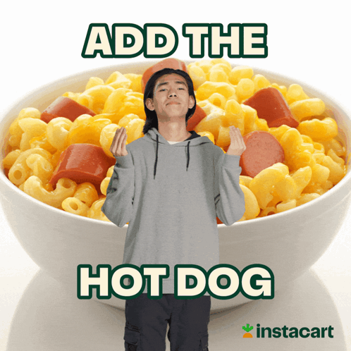 A Man Is Standing In Front Of A Bowl Of Macaroni And Cheese With Hot Dogs GIF