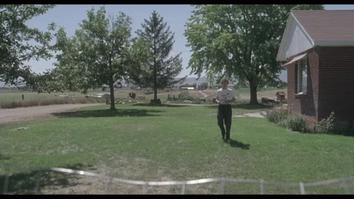 A Man Is Standing In Front Of A Brick House Holding A Piece Of Paper GIF