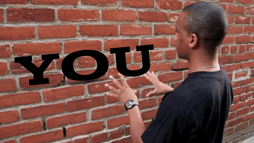 A Man Is Standing In Front Of A Brick Wall That Has The Word You Written On It GIF