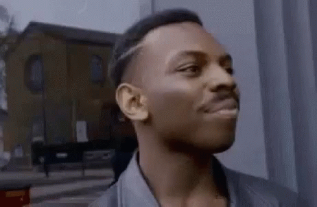 A Man Is Standing In Front Of A Building Looking At The Camera . GIF