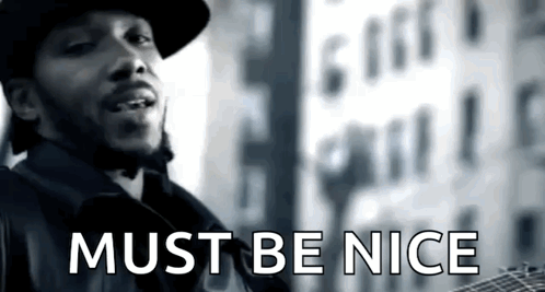 A Man Is Standing In Front Of A Building With The Words Must Be Nice On The Bottom GIF