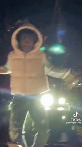 A Man Is Standing In Front Of A Car At Night . GIF