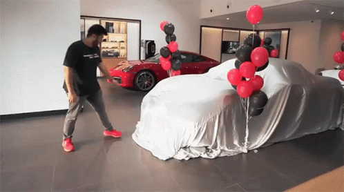 A Man Is Standing In Front Of A Car Covered In A Cloth GIF