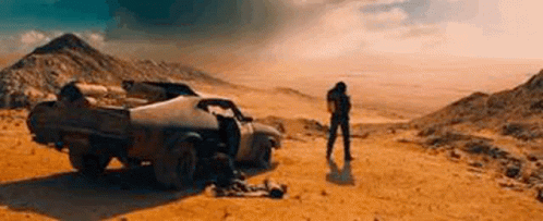 A Man Is Standing In Front Of A Car In The Desert . GIF