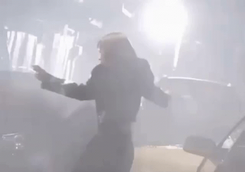 A Man Is Standing In Front Of A Car With His Arms Outstretched In A Foggy Room . GIF