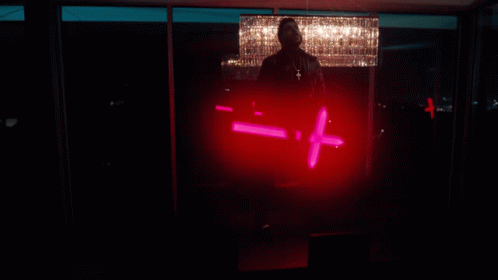 A Man Is Standing In Front Of A Chandelier And Holding A Red Light That Says - = + GIF