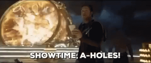 A Man Is Standing In Front Of A Clock And Says Showtime A-Holes GIF