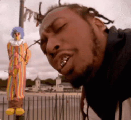 A Man Is Standing In Front Of A Clown Statue With His Eyes Closed GIF