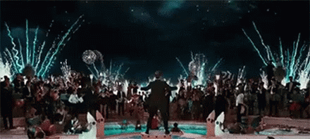 a man is standing in front of a crowd of people at a party with fireworks going off in the background .