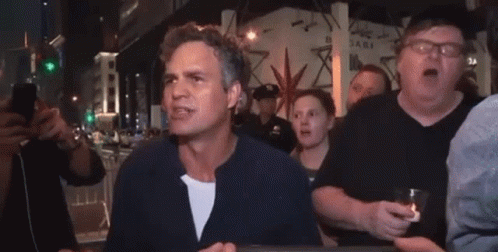 A Man Is Standing In Front Of A Crowd Of People Holding A Glass Of Beer . GIF
