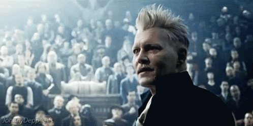 A Man Is Standing In Front Of A Crowd Of People In A Dark Room . GIF