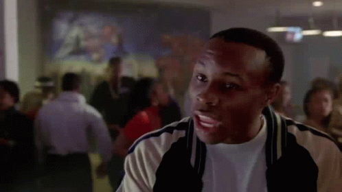 A Man Is Standing In Front Of A Crowd Of People In A Room . GIF