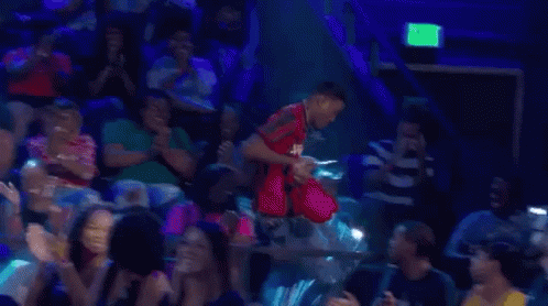 A Man Is Standing In Front Of A Crowd Of People In A Stadium . GIF