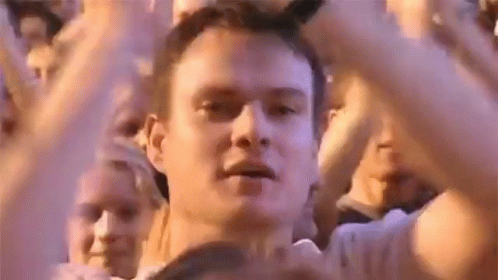 A Man Is Standing In Front Of A Crowd Of People With His Hands In The Air At A Concert . GIF