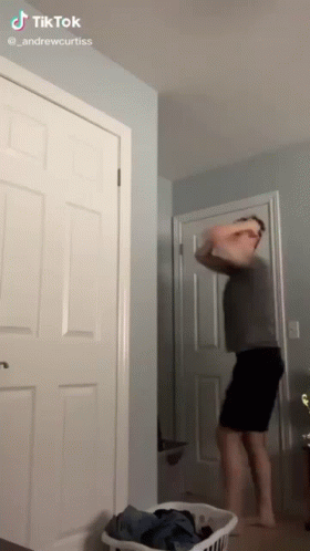 A Man Is Standing In Front Of A Door And A Laundry Basket In A Bathroom .. GIF