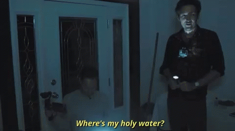 A Man Is Standing In Front Of A Door Holding A Flashlight And Asking Where Is My Holy Water . GIF