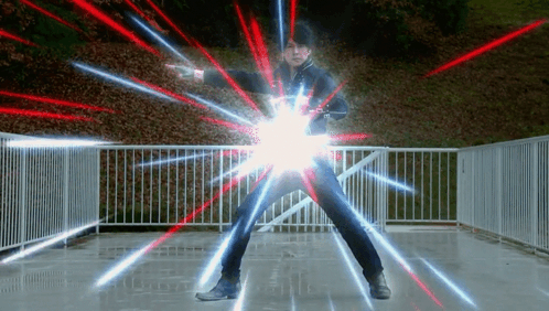 A Man Is Standing In Front Of A Fence With Red And Blue Lights Coming Out Of His Arms . GIF