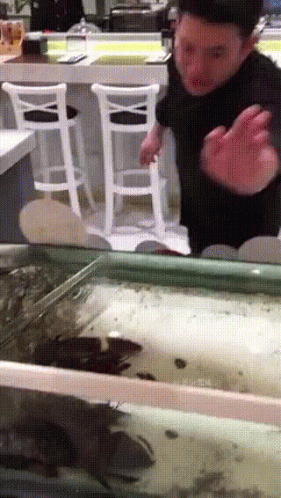 A Man Is Standing In Front Of A Fish Tank With A White Chair In The Background GIF