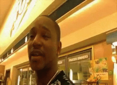 A Man Is Standing In Front Of A Frozen Dinners Sign In A Store . GIF