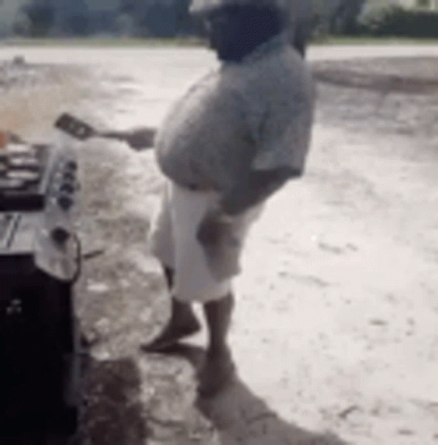 A Man Is Standing In Front Of A Grill Holding A Spatula And A Spoon . GIF