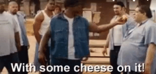 A Man Is Standing In Front Of A Group Of Men And Holding A Piece Of Cheese . GIF