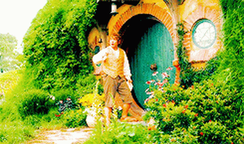 A Man Is Standing In Front Of A Hobbit House In The Woods . GIF