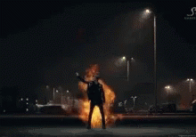 A Man Is Standing In Front Of A Huge Explosion Of Fire . GIF